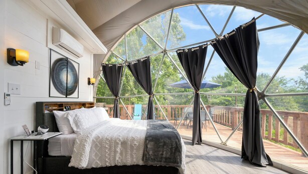 Un dormitorio con un ventanal grande, una cama, una mesita de noche y vistas al exterior.