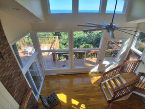 Habitación con techos altos, ventanas amplias, una terraza de madera y una escalera.