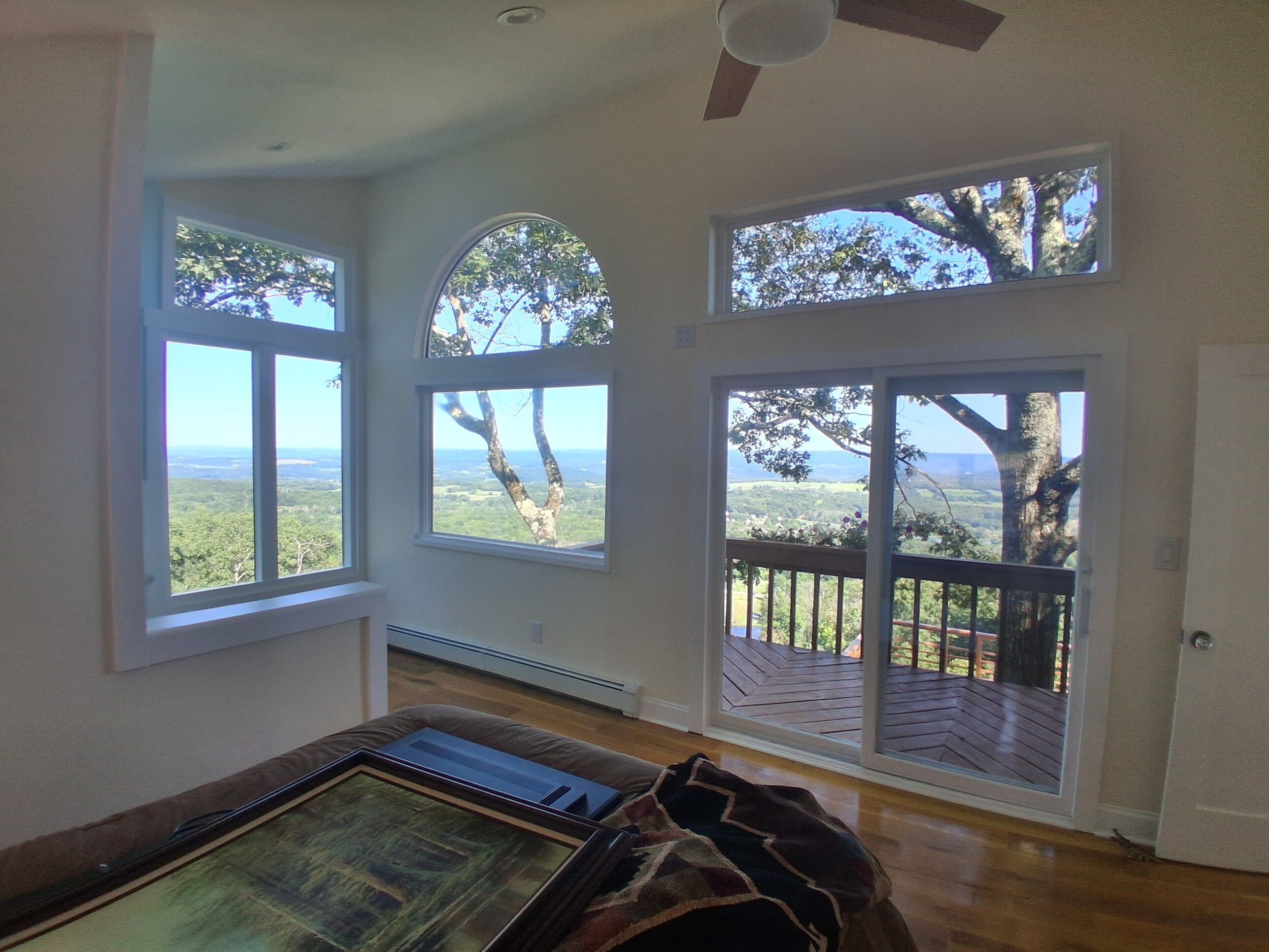 A room with large windows, a ceiling fan, and a view of the outdoors.