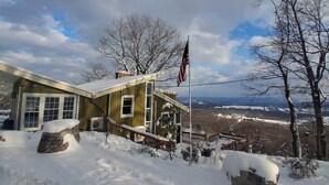 Una casa con techo nevado, un asta con la bandera estadounidense y una vista de paisaje invernal.