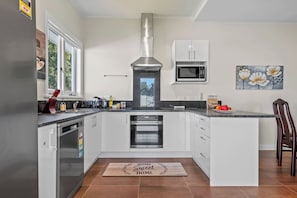 A kitchen with white cabinets, a stainless steel range hood, a microwave, and a wooden island with a 'HOME Sweet HOME' mat. - Family Comfort with Aircon, Backyard and Parking (Auckland South)
