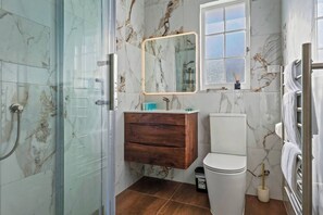 Ein Badezimmer mit einer gläsernen Duschkabine, einem Holzlagerflächen, einer weißen Toilette und einer Wand mit Marmorfliesen.