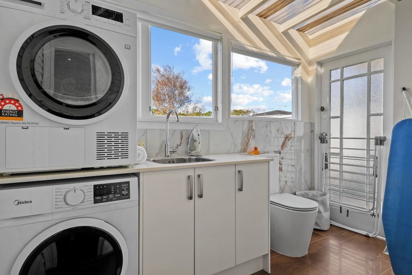 A compact laundry room with a washing machine, a dryer, a sink, and a window with a view of the outside.