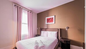 Hotelkamer met een bed, nachtkastje, lamp, foto aan de muur en een raam met gordijnen.