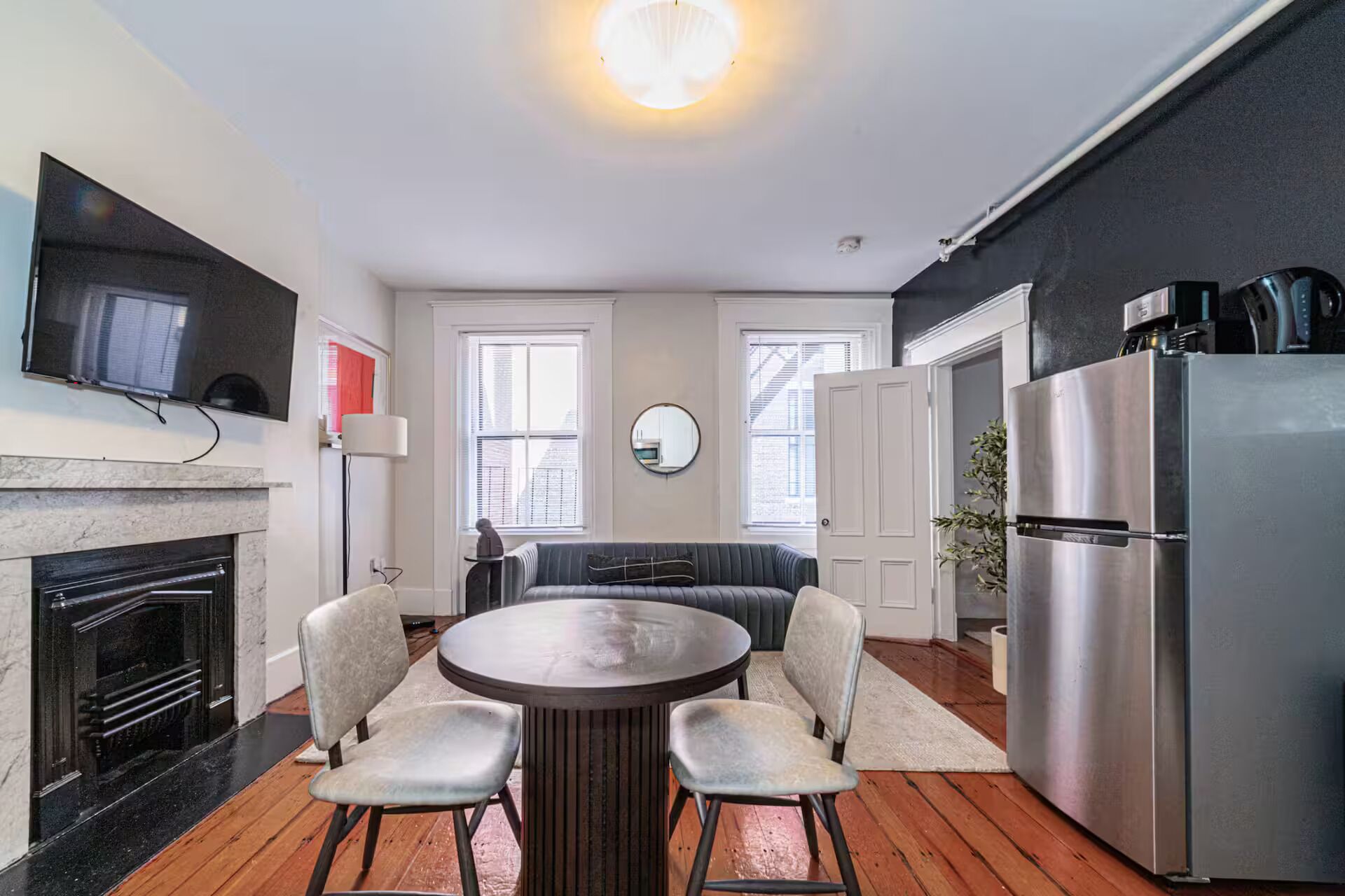 A modern kitchen with a dining area, a large refrigerator, and a flat-screen TV mounted on the wall.