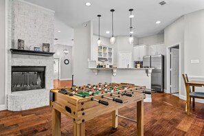 Ein modernes Wohnzimmer mit Tischfußball, Kamin und Küchenbereich.
