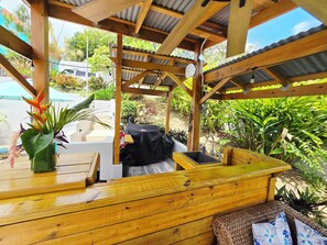 A wooden outdoor seating area with a grill, a sink, and a potted plant.