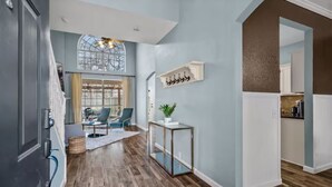A modern interior with a wooden floor, a glass coffee table, a blue wall, and a kitchen area. - New Centrally Located North Richland Hills Home (North Richland Hills)