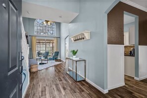 A modern interior with a wooden floor, a glass coffee table, a blue wall, and a kitchen area. - NEW Centrally Located North Richland Hills Abode (North Richland Hills)