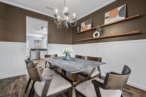Un comedor con una mesa de mármol, sillas, una araña y estanterías decorativas.