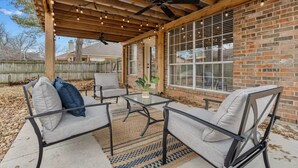 A covered patio with a ceiling fan, outdoor seating, and a brick wall. - New Centrally Located North Richland Hills Home (North Richland Hills)