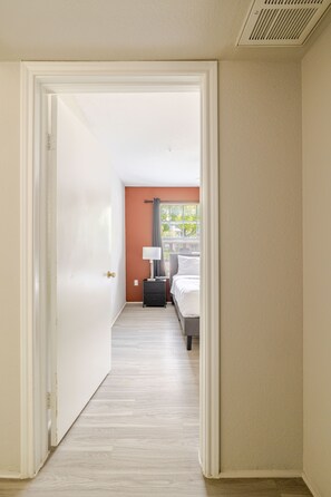 A hallway leading to a bedroom with a bed, nightstand, lamp, and window with curtains. - Best 1Bed 1Bath, 5 min walk to NRG /by Med Center (Houston)