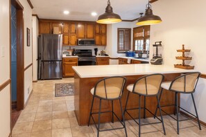 A kitchen with wooden cabinets, a stainless steel refrigerator, a large island with bar stools, and pendant lighting. - Wonderful 4-bedroom minutes from Trilith, QTS and U.S. Soccer Training Facility (Fayetteville)