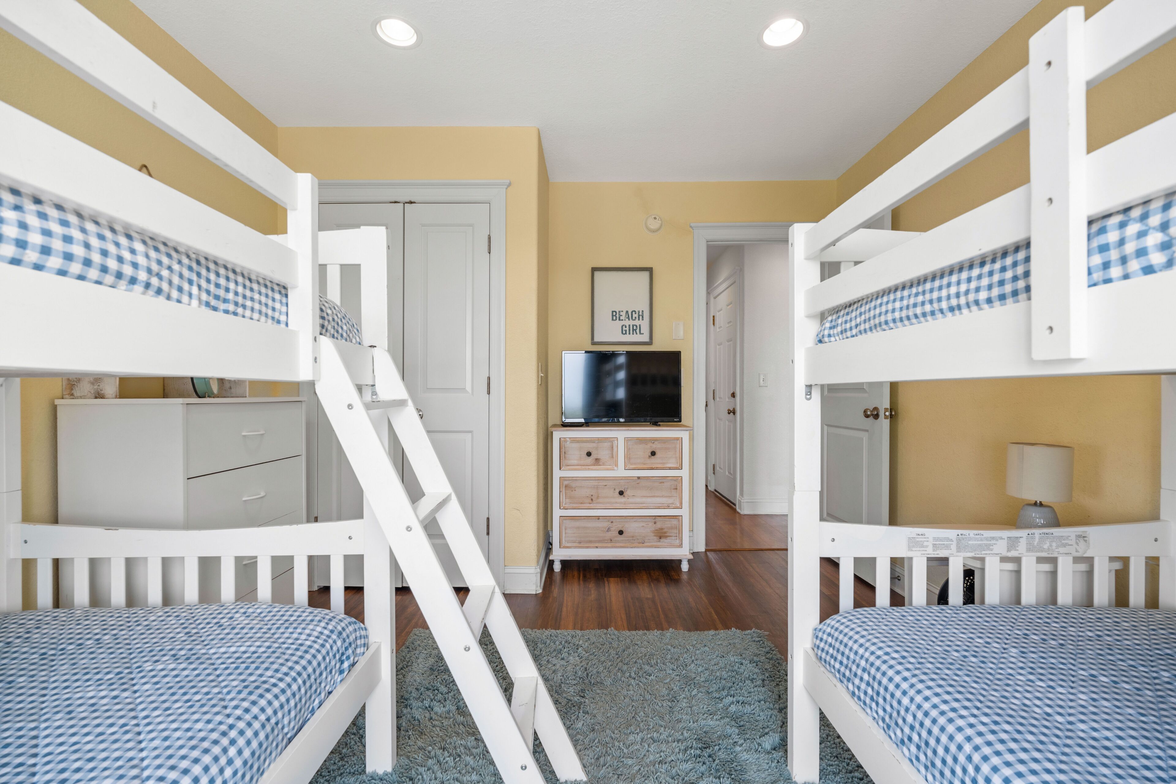 A room with bunk beds, a dresser, a television, and a door leading to another room.
