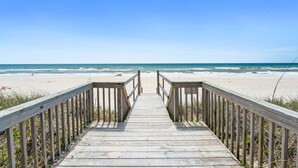 Ein hölzerner Steg führt zu einem Strand unter blauem Himmel.