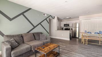 A modern living room with a grey sofa, a wooden coffee table, and a kitchen in the background.