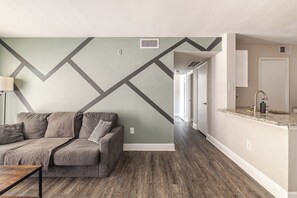 A modern living room with a geometric-patterned wall, a grey sofa, and a wooden floor. - Green King 2Bed 2Bath| walk to NRG| 1mi Med Center (Houston)