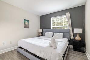 A modern bedroom with a large bed, two bedside tables with lamps, a window with blinds, and a single artwork on the wall. - Green King 2Bed 2Bath| walk to NRG| 1mi Med Center (Houston)
