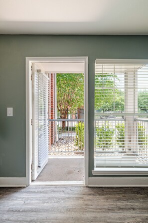 An interior space with a doorway leading to an outdoor area, a window with blinds, and a wooden floor. - Green King 2Bed 2Bath| walk to NRG| 1mi Med Center (Houston)
