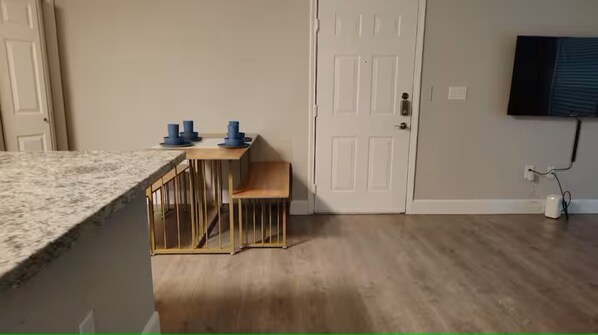 A kitchen with a granite countertop, a wooden dining table with chairs, a white door, and a wall-mounted television. - Comfy King 2Bed 2Bath /Walk to NRG/ 1mi Med Center (Houston)