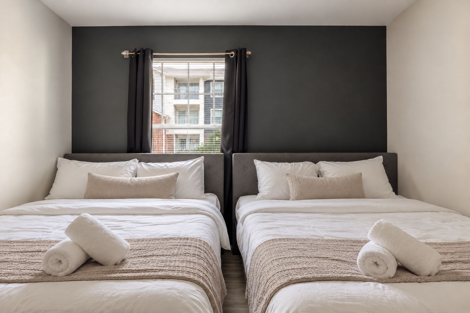 A hotel room with two beds, dark walls, and a window with curtains.