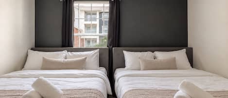 A hotel room with two beds, dark walls, and a window with curtains.