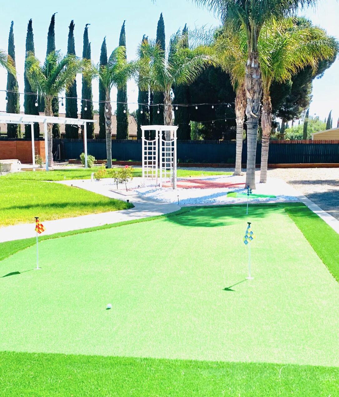 Un campo de golf con un putting green, un pabellón blanco y altas palmeras.