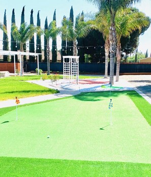 Ein Golfplatz mit Putting Green, einem weißen Gazebo und hohen Palmen.