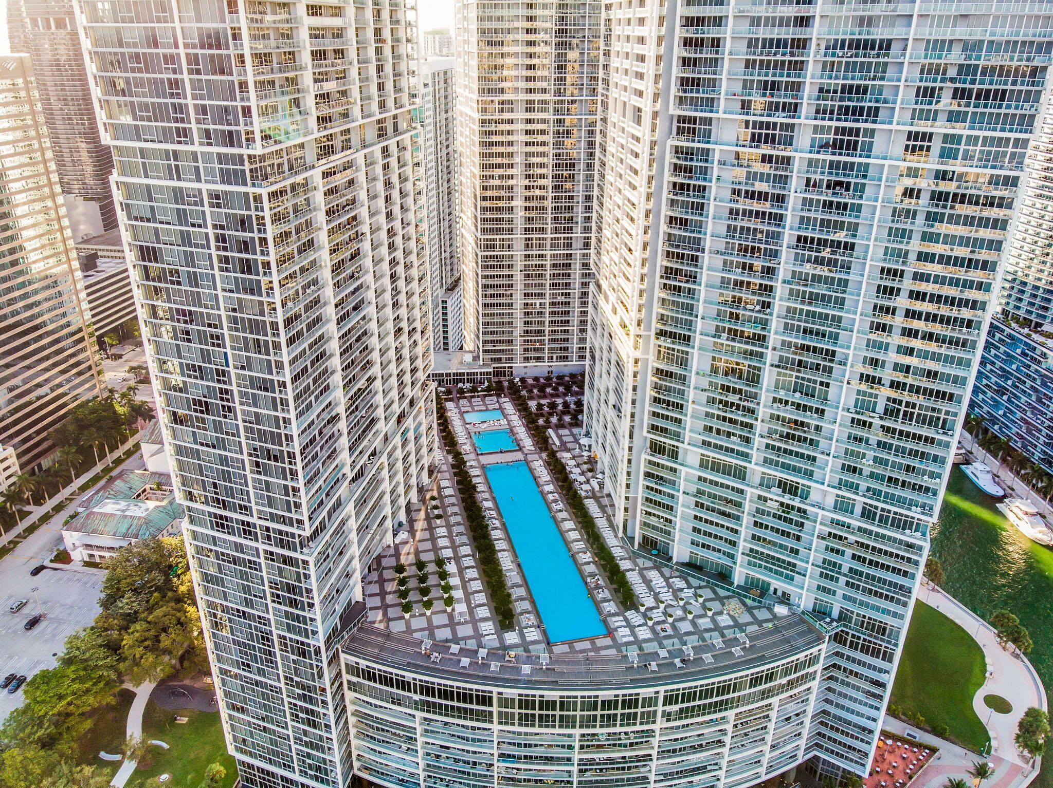 A high-rise building with a central courtyard featuring a swimming pool, surrounded by other high-rise buildings.