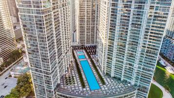 A high-rise building with a central courtyard featuring a swimming pool, surrounded by other high-rise buildings.