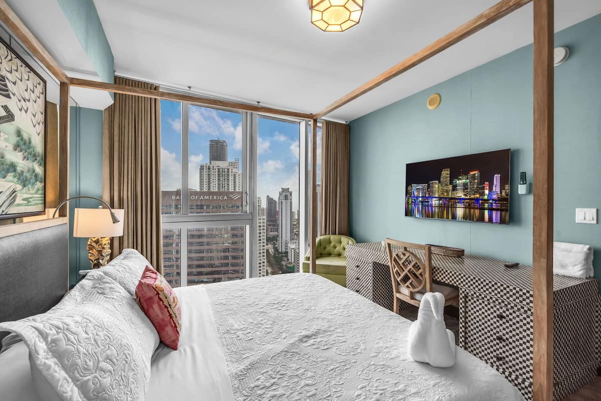 Habitación de hotel con una cama grande, un escritorio, una silla, un televisor y vistas a la ciudad.