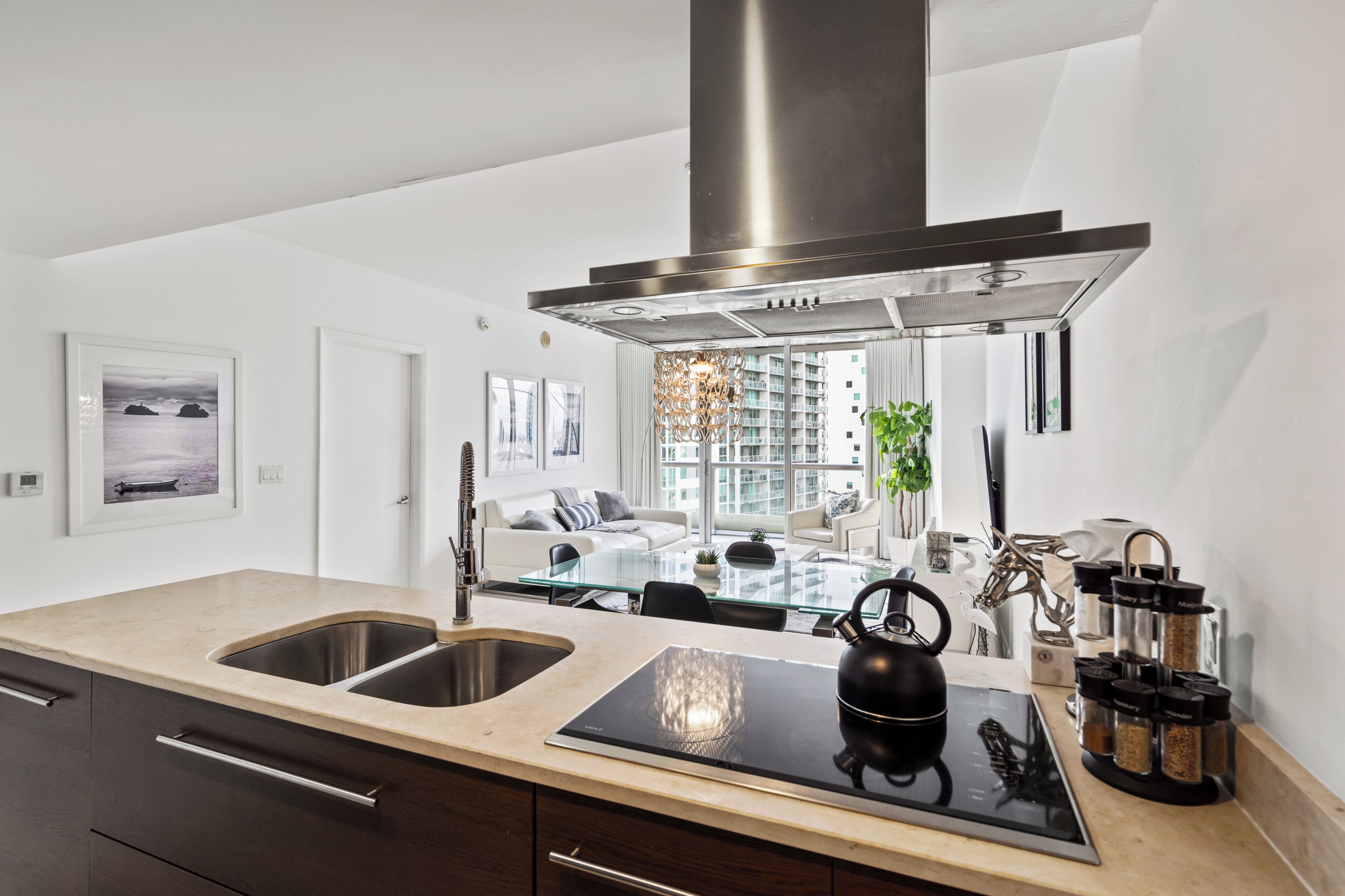 A modern kitchen with a stainless steel range hood, double sink, and a black induction cooktop.