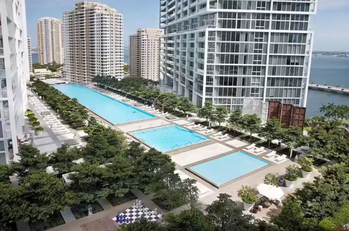 Un edificio de gran altura con piscina en la azotea, rodeado de vegetación y otros edificios altos.