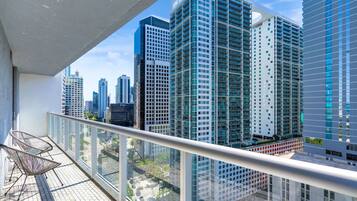 A balcony with a glass railing, a chair, and a view of high-rise buildings.