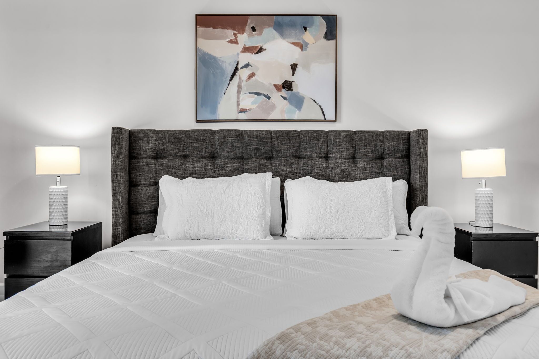 Une chambre d’hôtel avec un grand lit, deux tables de chevet avec des lampes et une peinture abstraite moderne accrochée au mur.