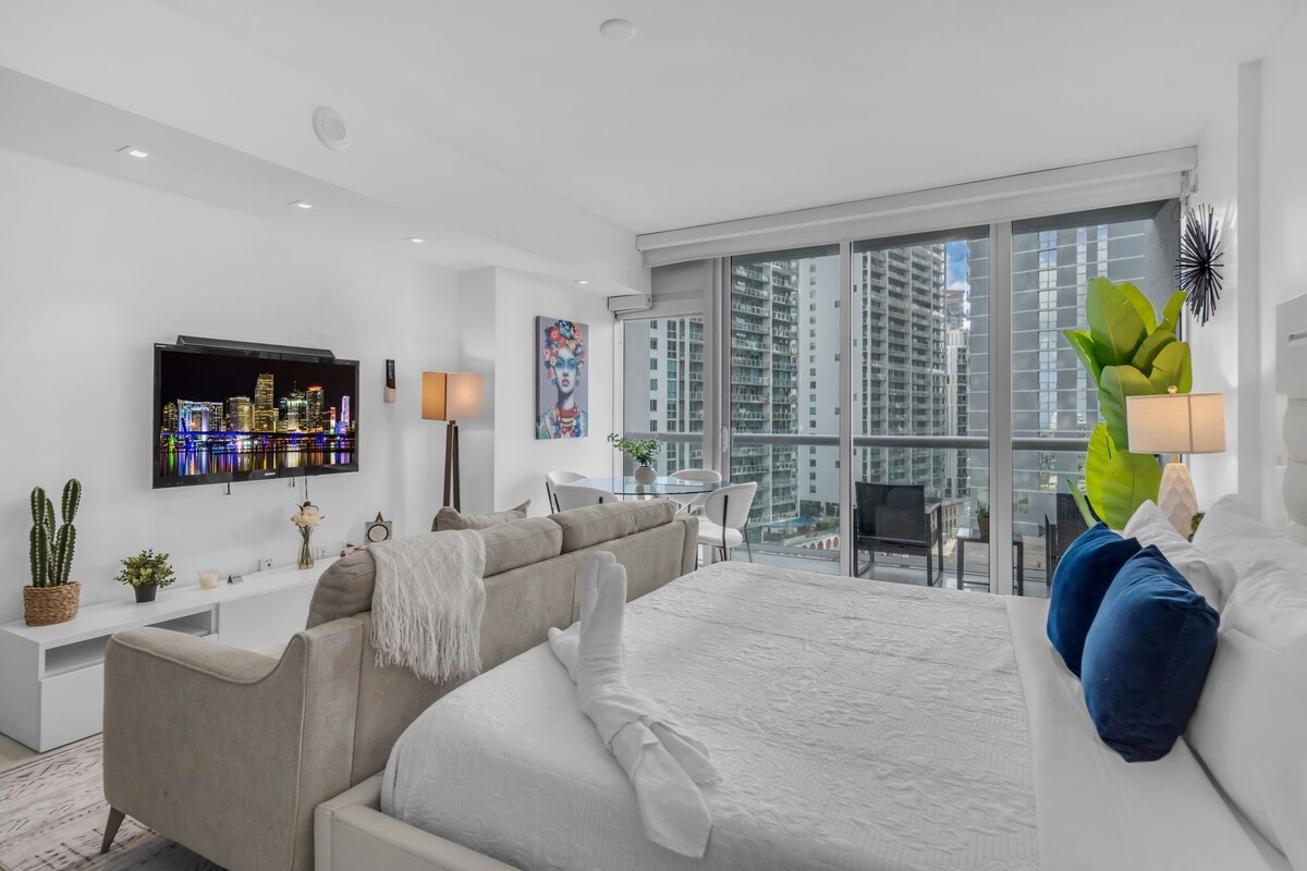 Une chambre d’hôtel moderne équipée d’un lit, d’un canapé, d’une télévision, d’un balcon avec vue sur la ville et d’un coin repas.
