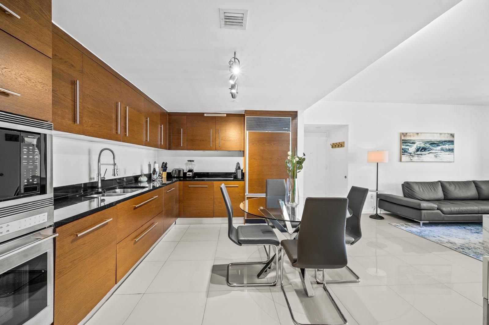 Eine moderne Küche mit Holzschränken, ein Essbereich mit einem Glastisch und ein Wohnzimmer mit einer Couch.