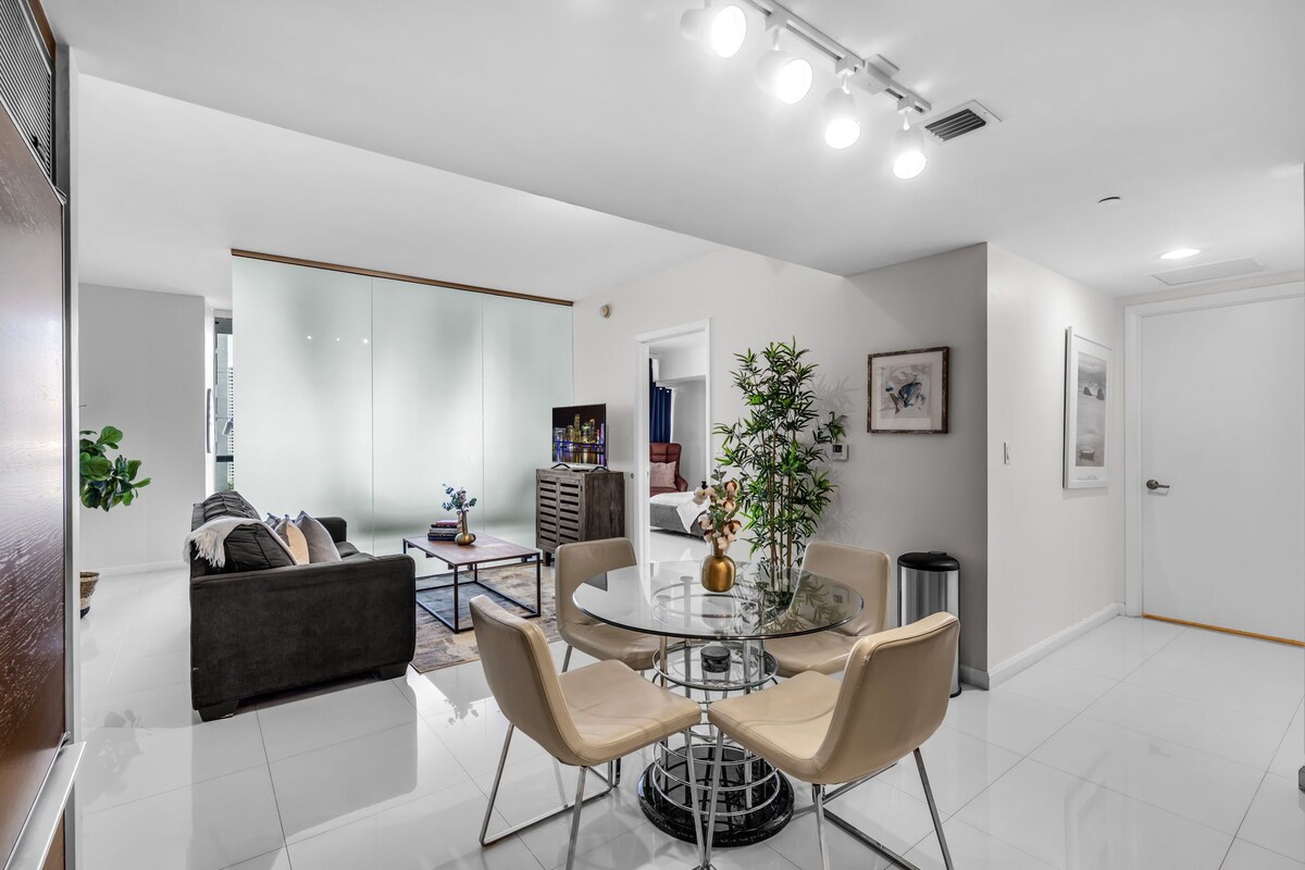A modern living room with a glass dining table, a sofa, and a TV.
