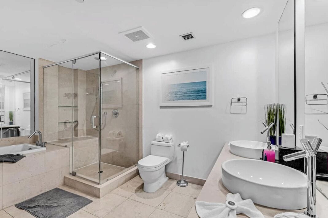 A modern bathroom with a glass-enclosed shower, a toilet, a sink, and a large mirror.