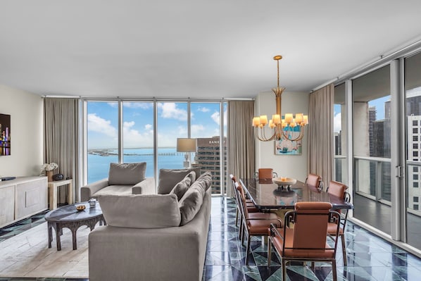 A spacious hotel room with a large balcony, a dining area, and a view of the sea.