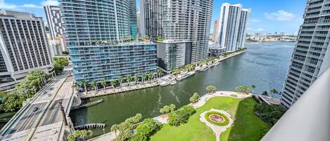 A high-rise urban area with modern buildings, a river, and a park with a circular lawn.