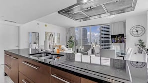 Una cocina moderna con una isla central, electrodomésticos de acero inoxidable y un comedor con vistas a la ciudad.