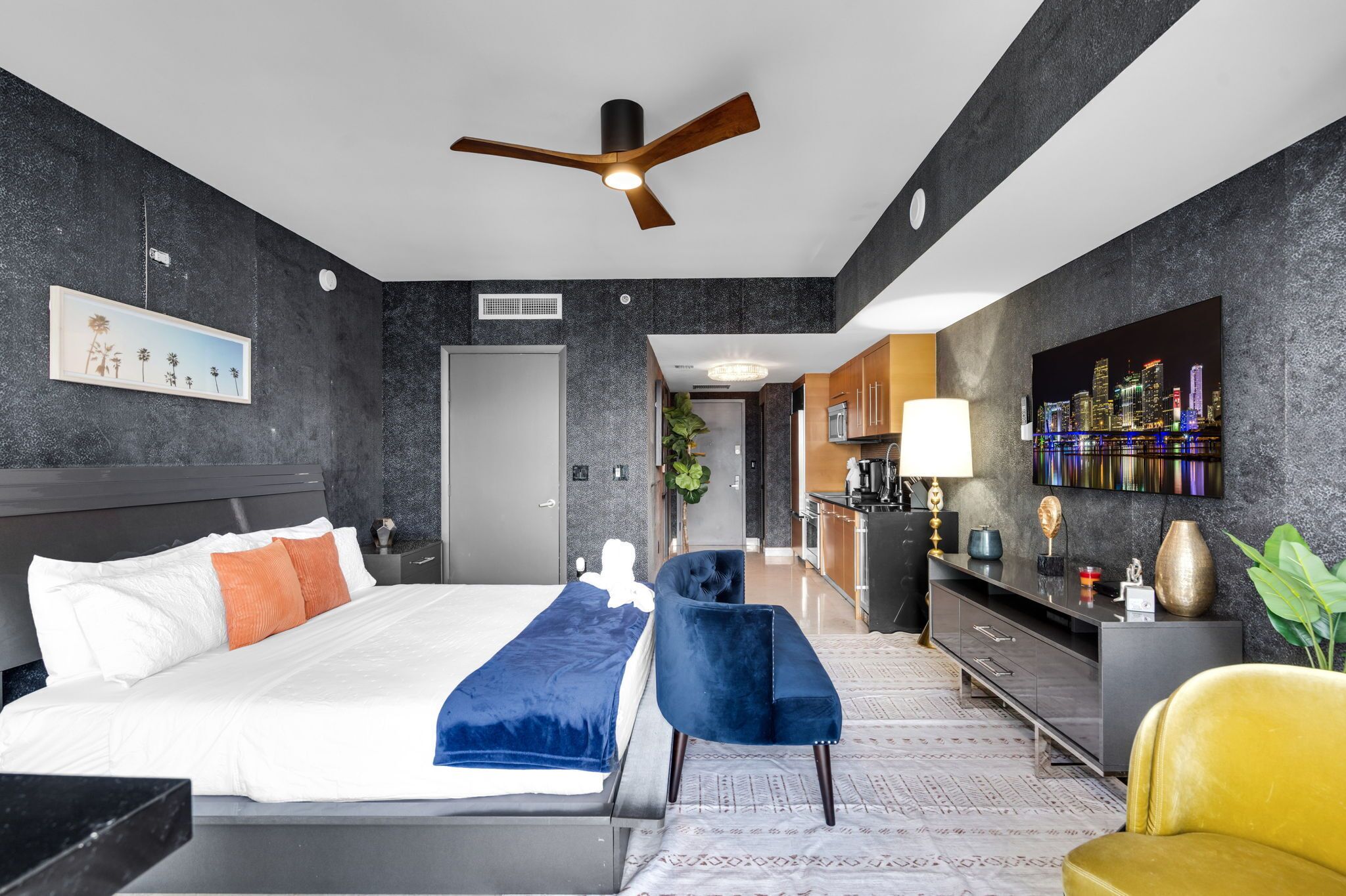 A modern hotel room with a bed, a desk, a chair, a TV, and a cityscape painting.