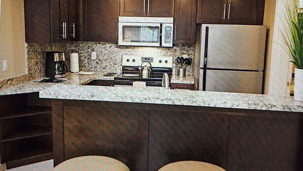 A kitchen with dark cabinets, a microwave, a stove, a refrigerator, and two stools.