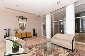 Lobby seating area with patterned beige sofas, glass coffee table, Persian-style rug, and large white columns. - The Pierre 906 by FGC (Longboat Key)