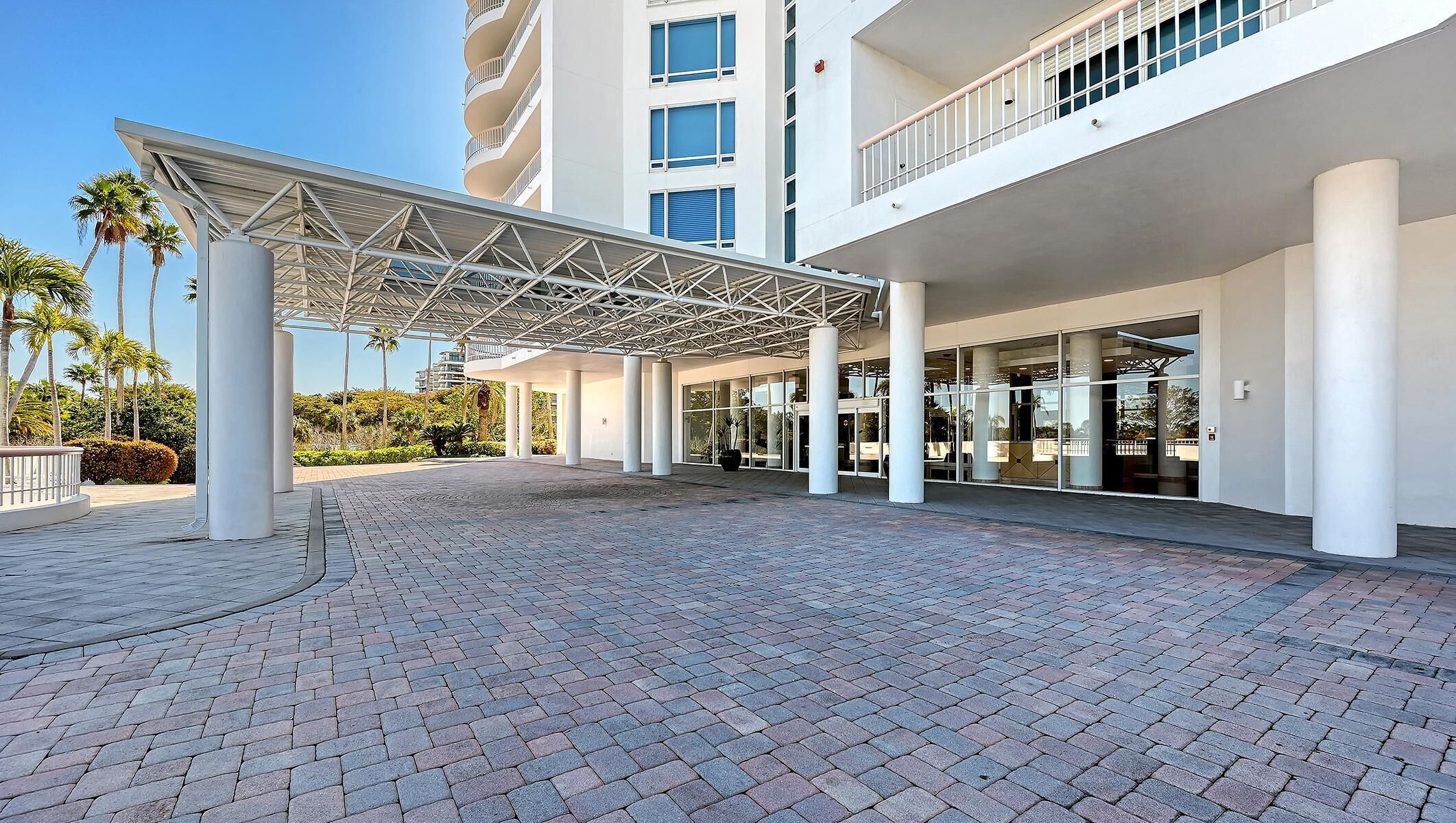 Covered porte-cochere with white columns and metal truss canopy over interlocking brick driveway.