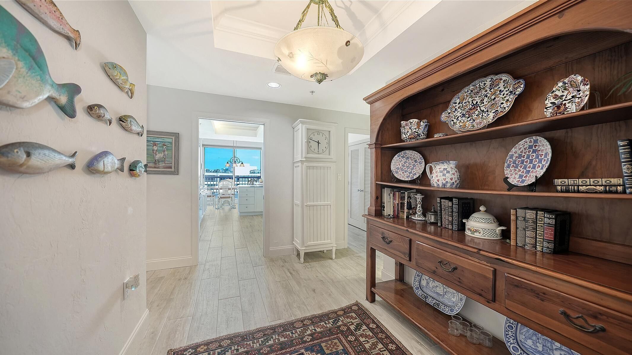 Entryway features wood-look tile flooring, a traditional wooden hutch with decorative plates, and a wall clock.