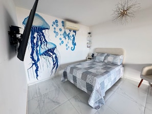 Une chambre à coucher comprenant un lit, un téléviseur fixé au mur, un luminaire au plafond et un élément décoratif mural.