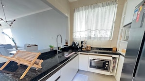 A modern kitchen with a black countertop, stainless steel appliances, a built-in oven, and a window with lace curtains. - Casa com rea Gourmet Piscina e Vista do Mar (Canguaretama)