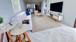 A modern living room with a sofa, TV, dining table, and kitchen in the background. - Casa com rea Gourmet Piscina e Vista do Mar (Canguaretama)